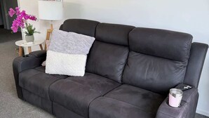 A dark brown leather sofa with a white throw pillow and a remote control on the armrest. - Bedroom (Jack's Point)