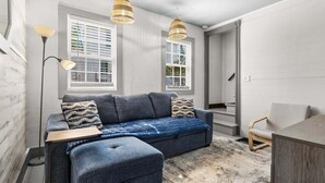 A modern living room with a sofa, ottoman, and a dining area. - Winter Harbor Haven - NEW! (Winter Harbor)