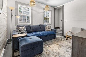 A modern living room with a sofa, ottoman, and a dining area.