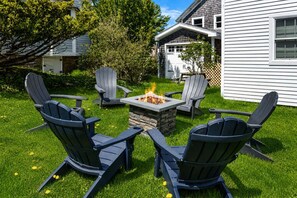 A backyard with a stone fire pit surrounded by four Adirondack chairs.