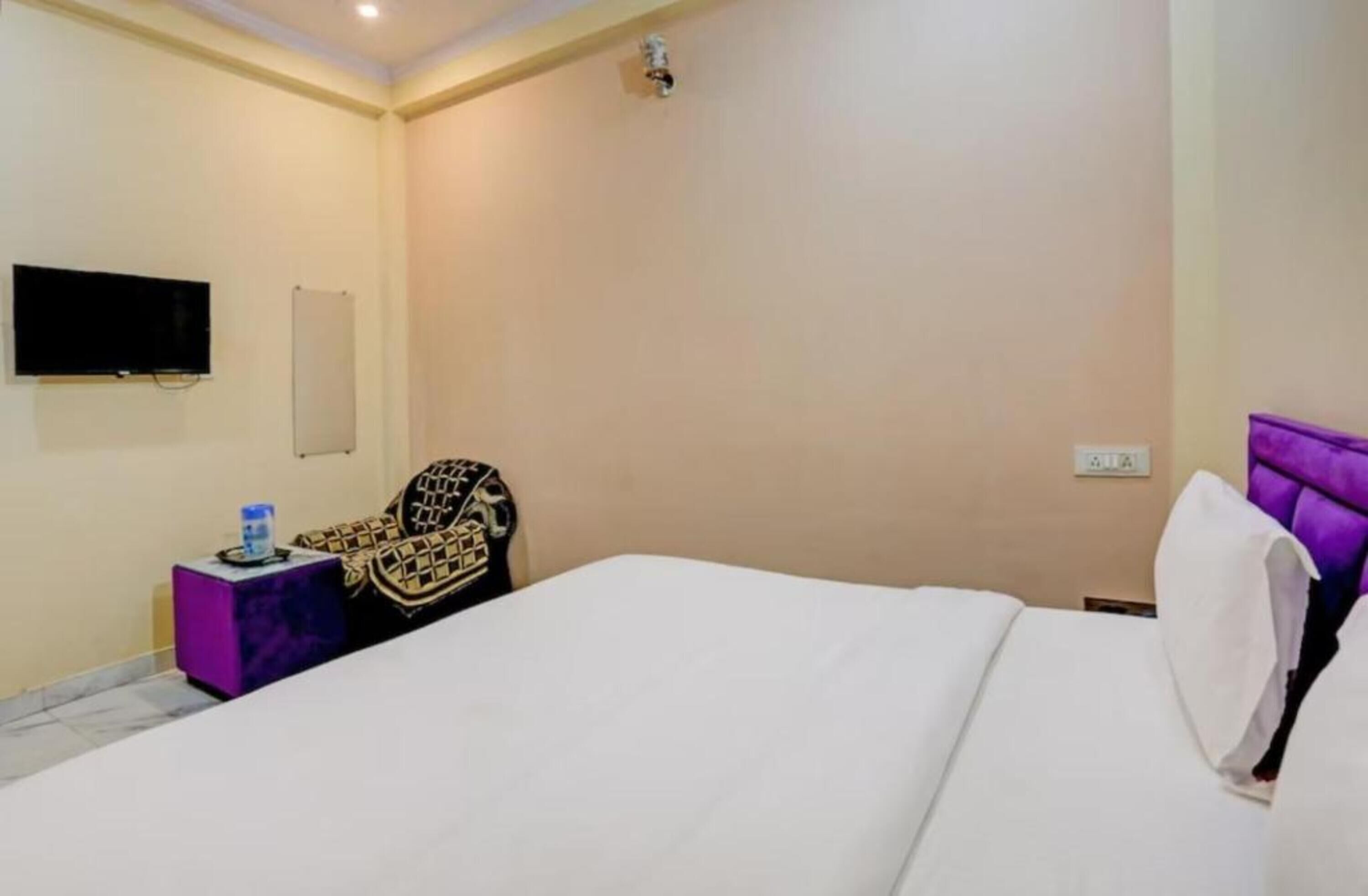 Una habitación de hotel con una cama, televisión, una silla y una mesita con una botella de agua.