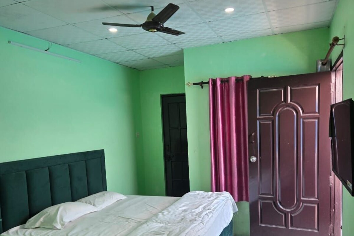 A room with two beds, a ceiling fan, a door, and a small table with a water bottle.