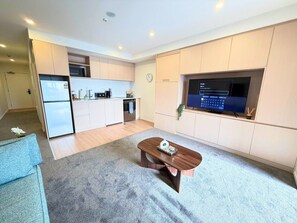 Ein modernes Wohnzimmer mit einer Couch, einem Couchtisch, einer Küchenzeile mit Schränken, einem Fernseher und einer Wanduhr.