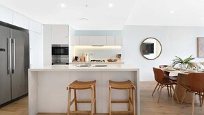 Een moderne keuken met een centraal eiland, roestvrijstalen apparatuur en een eethoek met houten stoelen en een tafel.