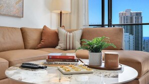 Een moderne woonkamer met een bank, een salontafel met afstandsbedieningen, boeken, een plant en een kaars.