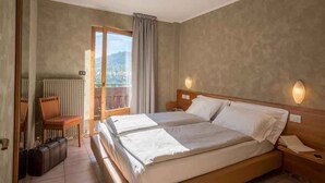 Ein Doppelbett mit hölzernem Kopfteil, ein Stuhl, ein Schreibtisch und ein Koffer in einem Zimmer mit Blick.