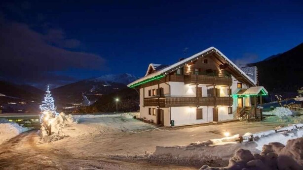 Schneebedeckte Landschaft mit einem zweistöckigen Gebäude mit Balkonen und einer beleuchteten Außenfassade.