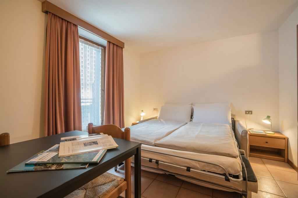 Une chambre d’hôtel avec un lit, des tables de chevet, un bureau avec des papiers et une fenêtre avec des rideaux.