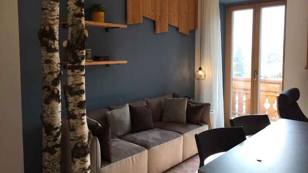 A modern living room with a sectional sofa, a dining table, and a wooden shelf. - Studio with terrace and mountain view (Cavedago)