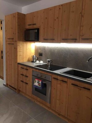 A modern kitchen with wooden cabinets, a microwave, a stove, and a sink. - Holiday apartment with mountain view and terrace (Cavedago)