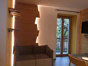 A modern living room with a sofa, a dining table, and a TV mounted on the wall. - Holiday apartment with mountain view and terrace (Cavedago)