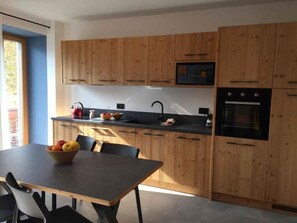 A modern kitchen with wooden cabinets, a black countertop, and a dining table with chairs. - Holiday apartment with mountain view and terrace (Cavedago)
