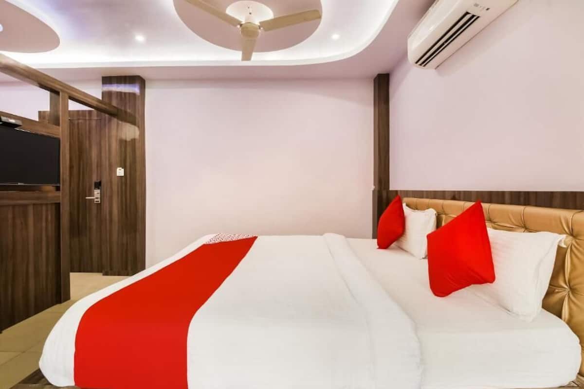A hotel room with a bed, a ceiling fan, an air conditioning unit, and a wooden panel wall.