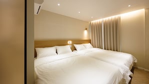 Une chambre d’hôtel avec un grand lit, une tête de lit en bois, un climatiseur fixé au mur et une fenêtre avec des rideaux.