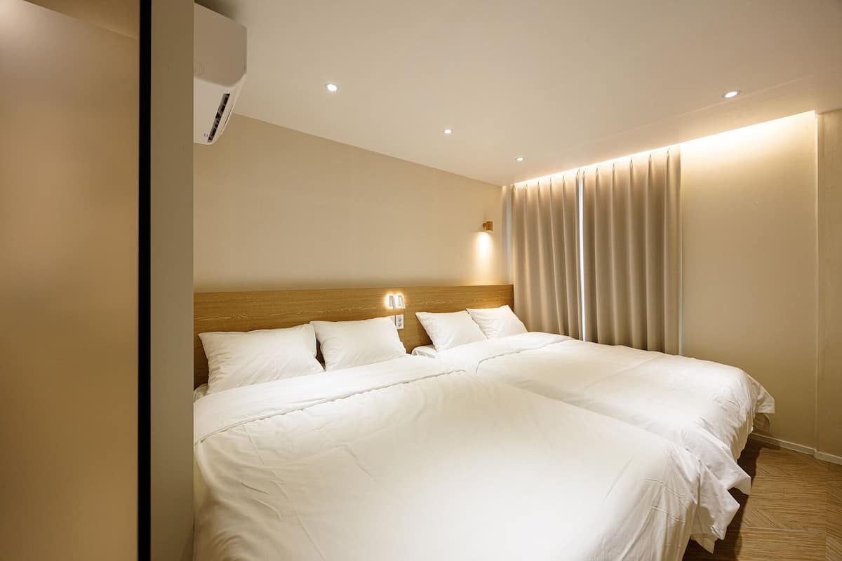 Habitación de hotel con una cama grande, cabecera de madera, aire acondicionado de pared y una ventana con cortinas.