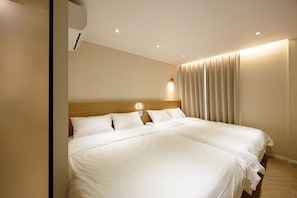 Hotellihuone, jossa on suuri sänky, puinen pääty, seinään asennettu ilmastointilaite ja ikkuna, jossa on verhot.