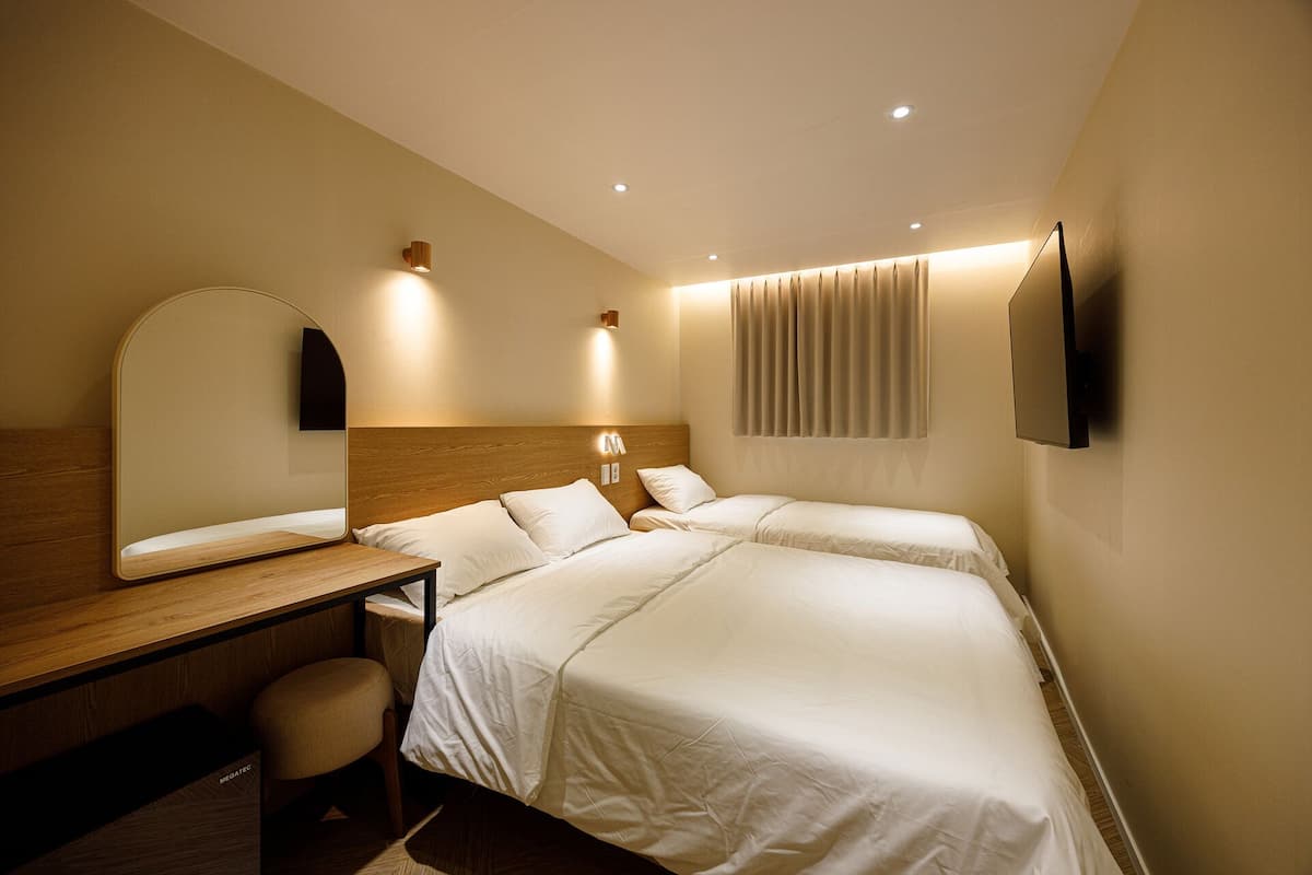 Habitación de hotel con dos camas, un escritorio, una silla, un espejo, un televisor de pantalla plana y una ventana con cortinas.