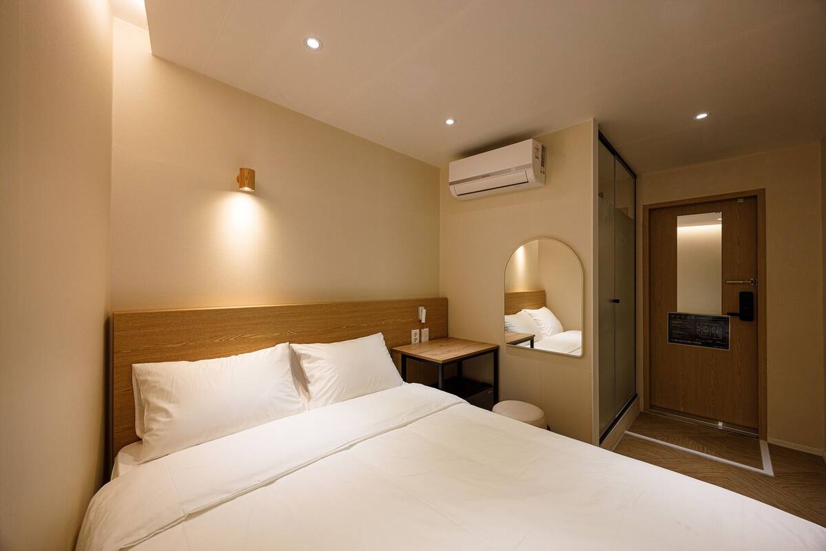 Habitación de hotel con cama, mesita de noche, espejo y equipo de aire acondicionado.