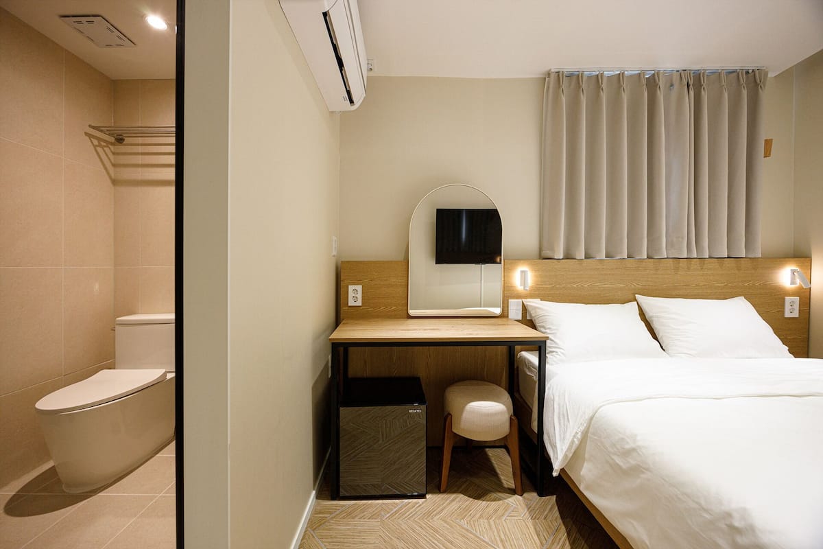 Habitación de hotel con inodoro, escritorio con espejo, cama y zona de ducha.