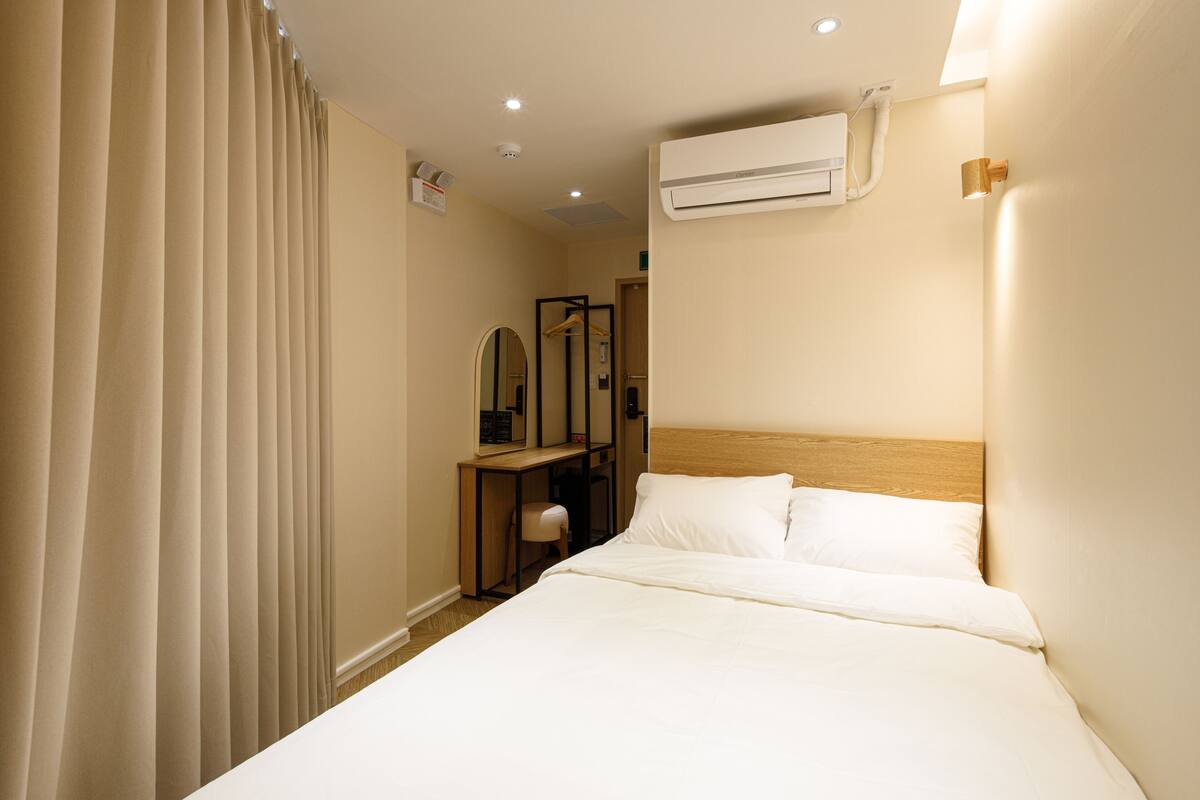 Una habitación de hotel con cama, unidad de aire acondicionado, escritorio con silla y espejo.