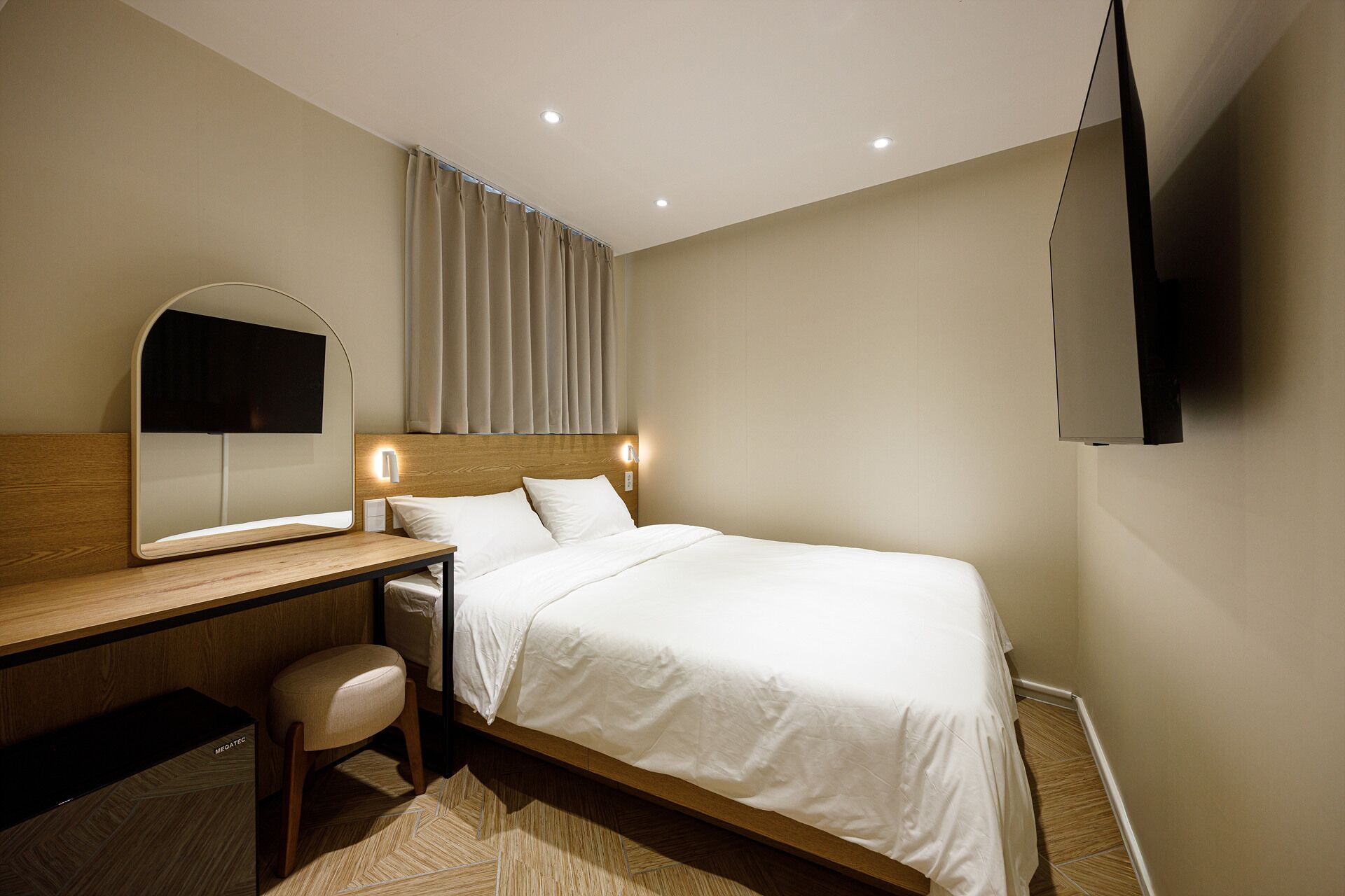 A hotel room with a bed, a desk, a chair, a mirror, a flat-screen TV, and a window with curtains.
