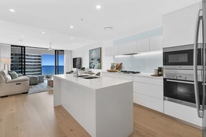 A modern kitchen with a central island, white cabinetry, and a view of the sea. - Ocean Views at Oracle Level 17 (Gold Coast)