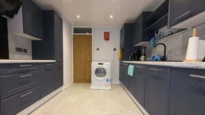 A modern kitchen with dark cabinets, a washing machine, and a countertop with a blender. - Room-budget Friendly Private Room - Your (Wellingborough)