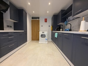 A modern kitchen with dark cabinets, a washing machine, and a countertop with a blender.