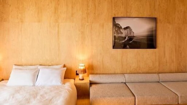 A bedroom with a wooden ceiling, a bed, a bench, and a wall-mounted picture.