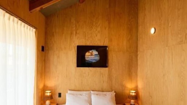 A large bed with two pillows, wooden beams on the ceiling, and two bedside lamps. - DEAR MOM (Onjuku)