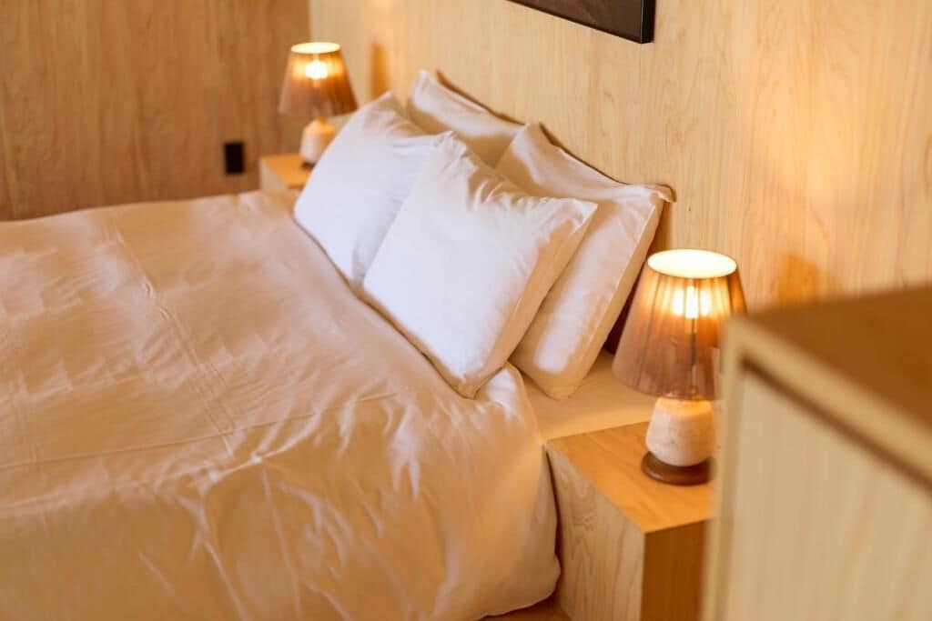 A neatly made bed with white linens and pillows, two bedside lamps, and a wooden headboard.