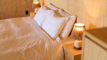 A neatly made bed with white linens and pillows, two bedside lamps, and a wooden headboard.