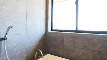 A bathroom with a bathtub, a window, and a shower.