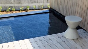 A small, rectangular pool with a wooden deck, a white pedestal, and a concrete wall in the background. - DEAR MOM (Onjuku)