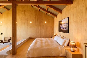 Un dormitorio con techo de madera, una cama con ropa blanca, una mesita de noche con lámpara y un cuadro enmarcado en la pared.