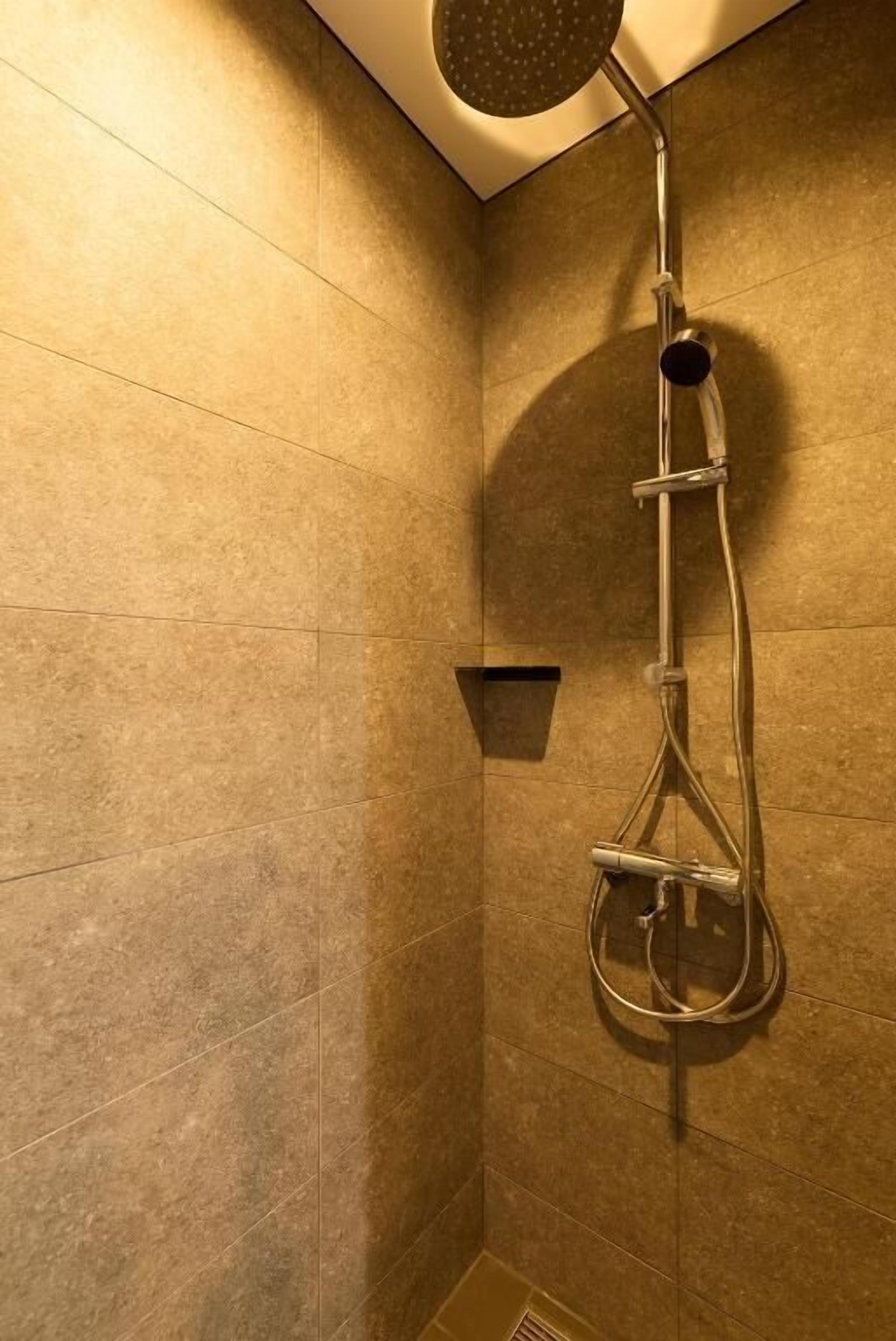 A shower with a handheld showerhead, a wall-mounted faucet, and a small shelf.