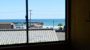 A view through a window of a coastal area with a beach, a pier, and a building with a tiled roof. - DEAR MOM (Onjuku)