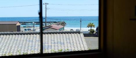 A view through a window of a coastal area with a beach, a pier, and a building with a tiled roof.