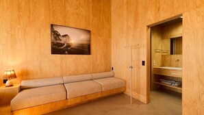 A wooden-paneled room with a sofa, a framed picture, a mirror, and a door leading to a bathroom.