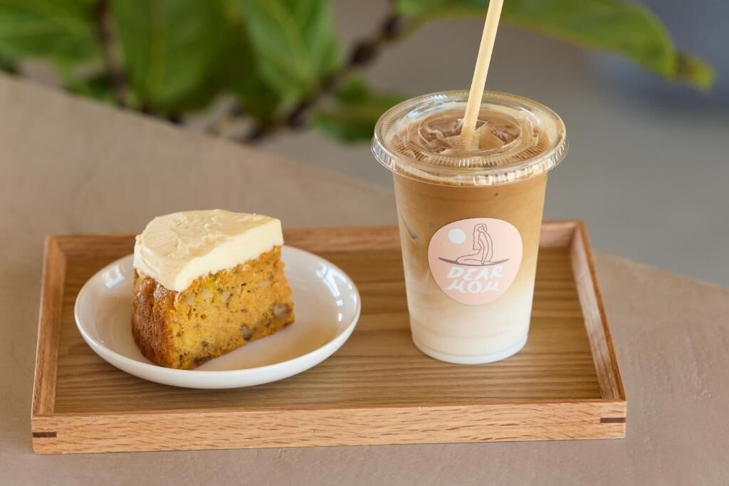 Una porción de pastel con glaseado sobre un plato, una bebida en un vaso de plástico con pajita, y un logotipo en el vaso.