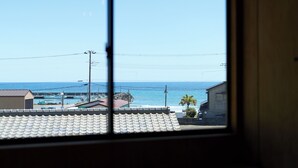 A coastal view through a window with a tiled roof, power lines, and buildings in the foreground.