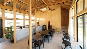 A spacious indoor area with wooden beams, tables, chairs, and large windows. - DEAR MOM (Onjuku)