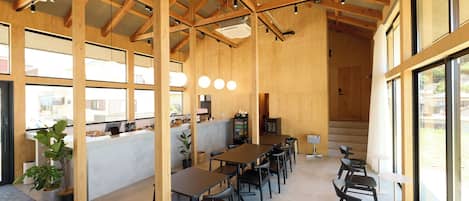 A spacious indoor area with wooden beams, tables, chairs, and large windows.