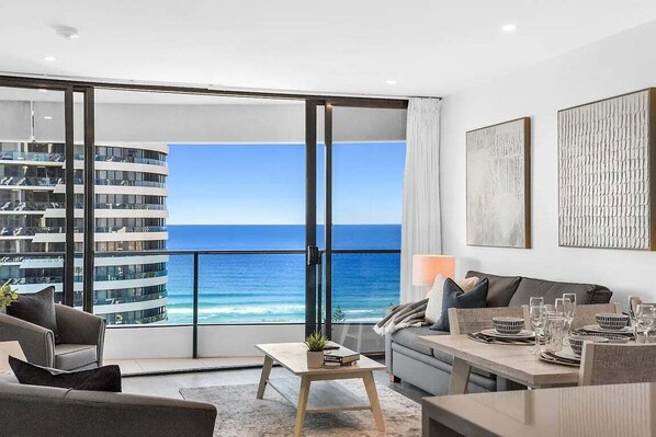 Ein modernes Wohnzimmer mit einem großen Schiebeglastür, die auf einen Balkon mit Blick aufs Meer und ein Hochhaus führt.