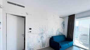 A modern room with a blue sofa, a white door, and a wall with a nature-themed mural. - Holiday flat with balcony (Lido di Jesolo)