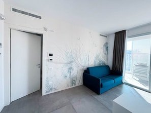 Ein modernes Zimmer mit einem blauen Sofa, einer weißen Tür und einer Wand mit einem Wandgemälde zum Thema Natur.