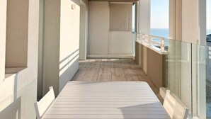 A balcony with a wooden floor, glass railings, and a view of the sea. - Holiday flat with balcony (Lido di Jesolo)