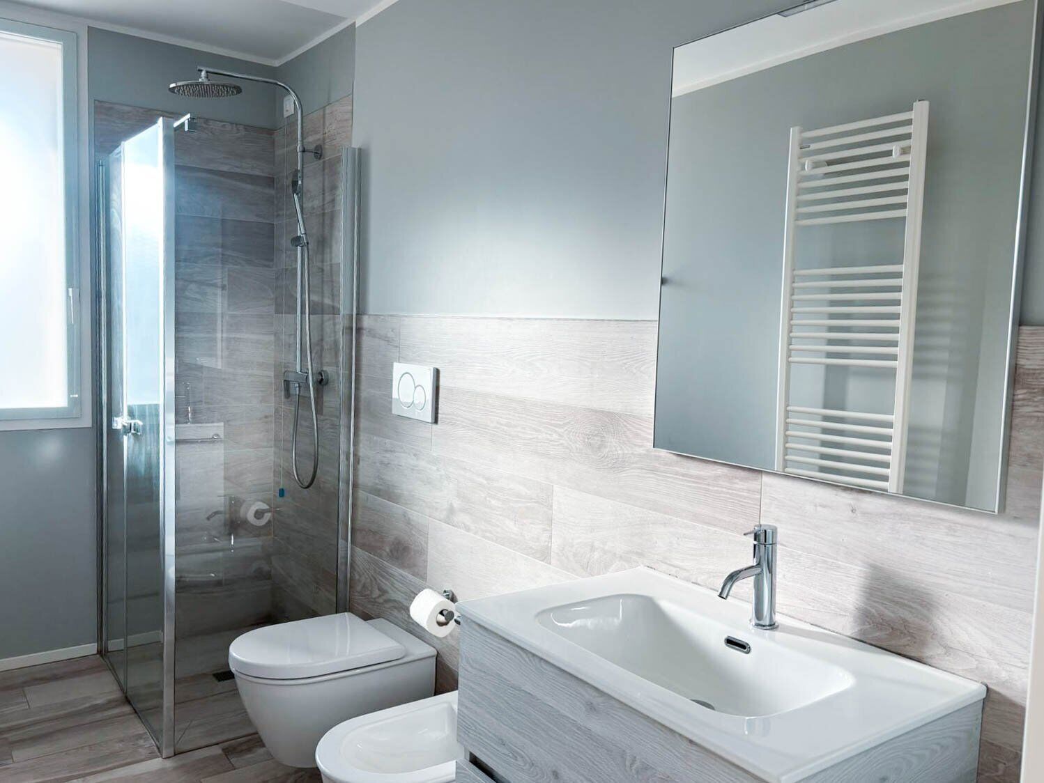 A modern bathroom with a glass shower enclosure, a toilet, a sink with a mirror, and a towel rack.
