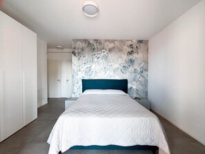 Ein Schlafzimmer mit Bett, Nachttisch, Wand mit Blumenmuster und einer Tür zu einem anderen Raum.