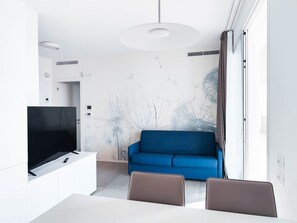 Ein modernes Wohnzimmer mit einem blauen Sofa, einem Flachbildfernseher und einem Essbereich mit Tisch und Stühlen.